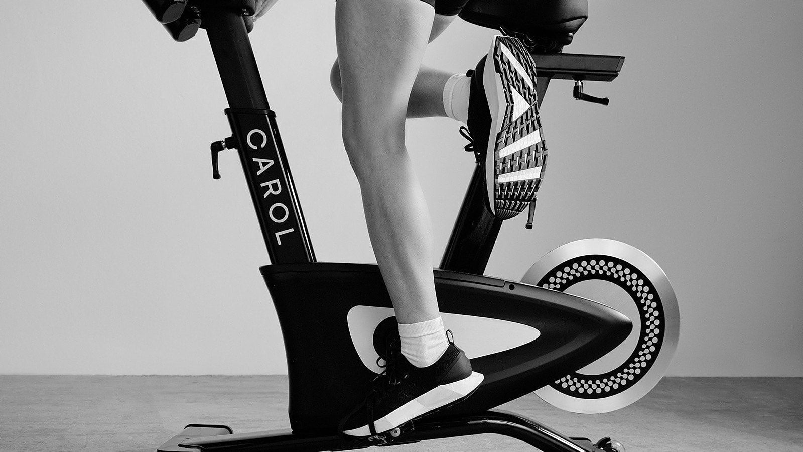 Foot driving the pedal of a CAROL Bike mid-sprint, black and white