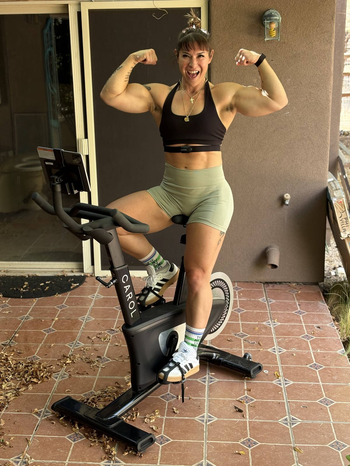 Kortney flexing both arms, one foot on the pedal of her CAROL Bike